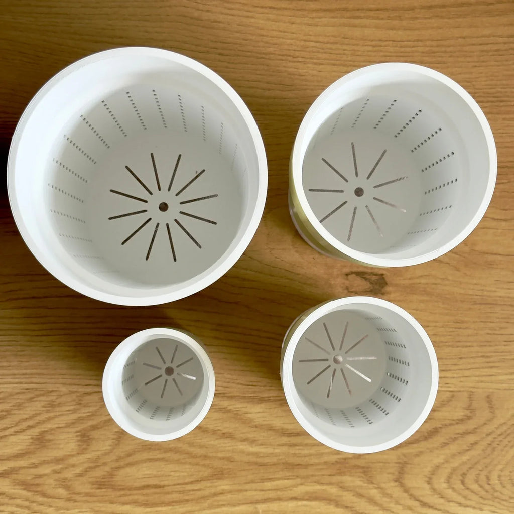 Set of white 3D printed plant pots with drainage holes on wood background, various sizes