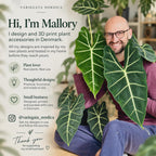 Variegata Nordica meet the maker slide showing the shop owner smiling among large green tropical leaves, with text explaining that the plant accessories are designed and 3D printed in Denmark, inspired by personal plant care experience, and inviting customers to follow @variegata_nordica.
